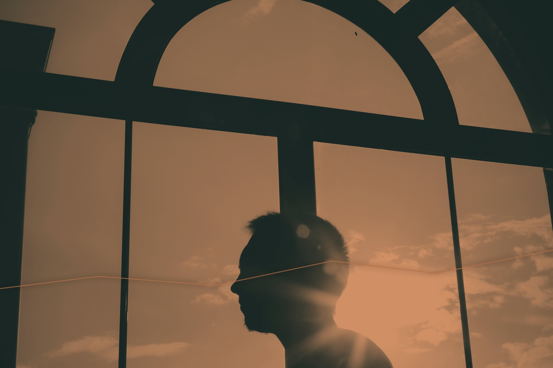A human silhouette looking through a large window toward warm evening light.
